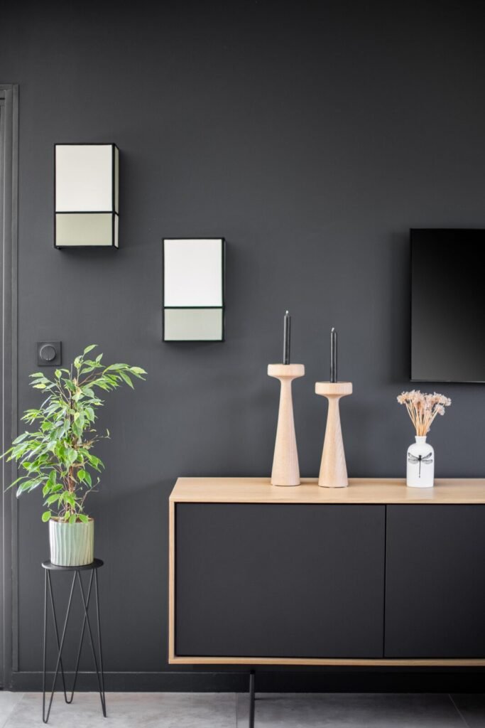 Détail de décoration : buffet en bois et noir, bougeoirs en bois et plante sur mur anthracite
