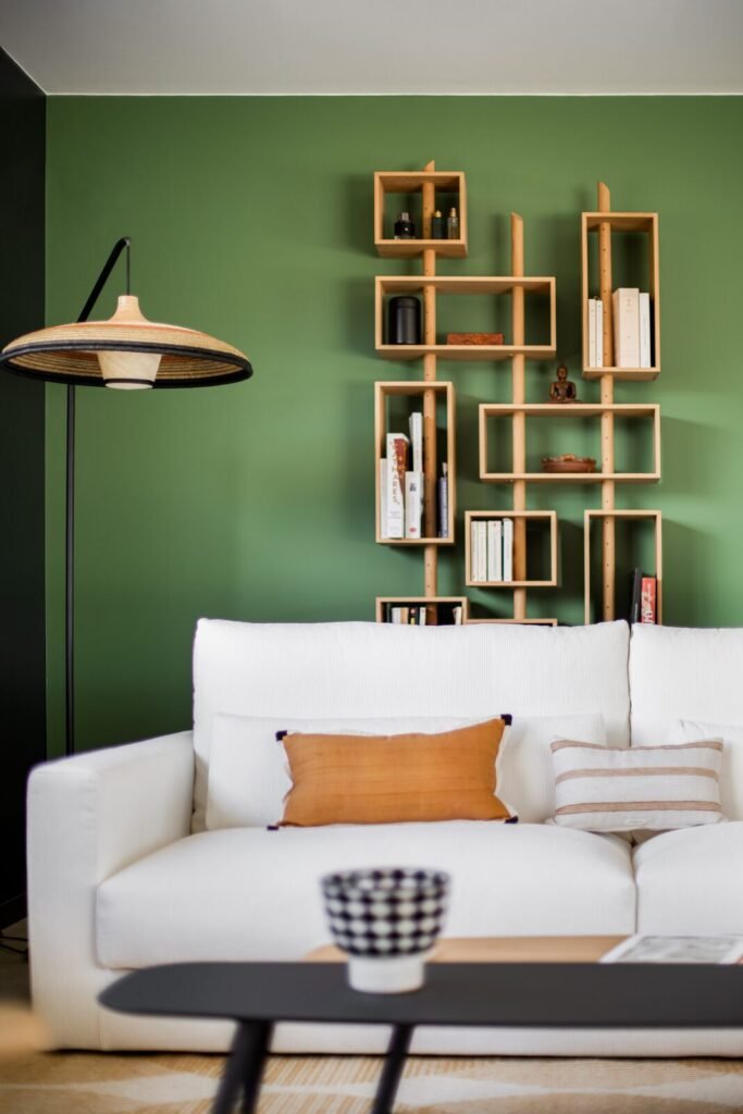 Canapé blanc, coussin orange et étagère modulaire en bois sur mur vert profond
