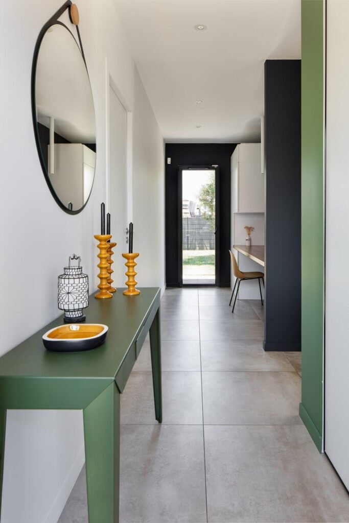 Entrée avec console verte, miroir rond et bougeoirs jaune moutarde, perspective vers le séjour