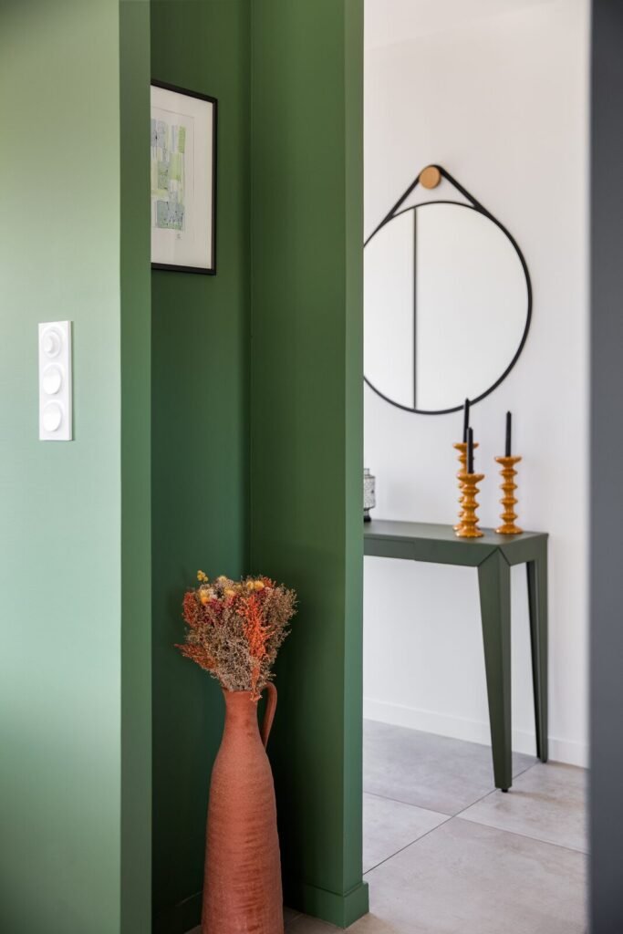 Entrée au mur vert profond, console, miroir rond et grand vase en terre cuite