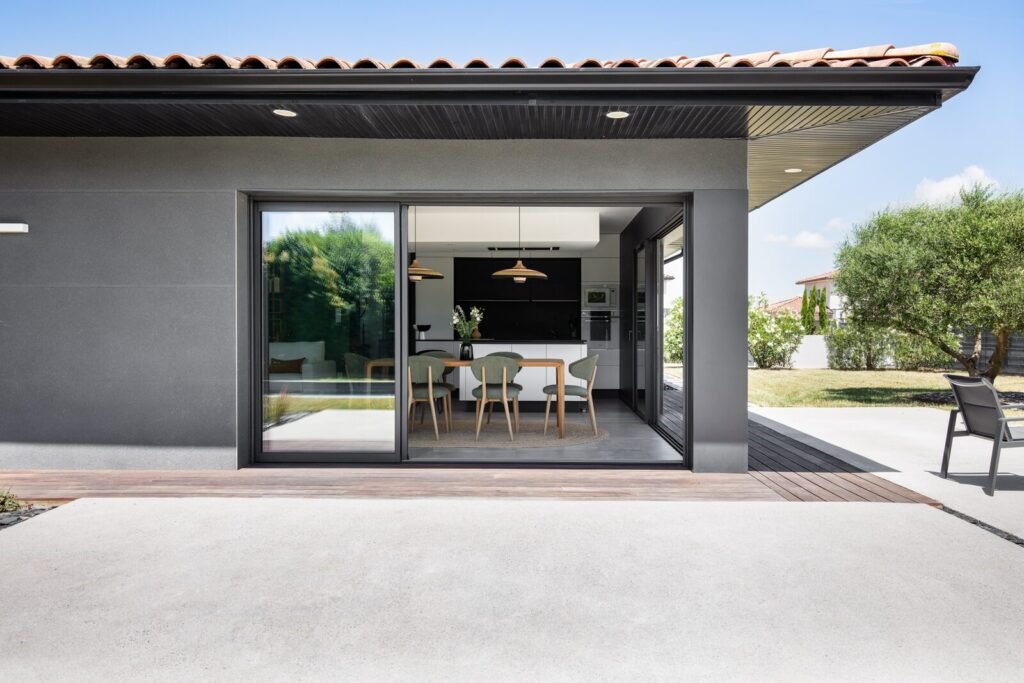 Terrasse couverte et baie coulissante ouverte sur la pièce de vie de la maison contemporaine